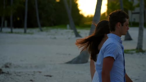 Golden hour light and silhouette of boy and girl holding hands, walking on tropical beach at sunset.