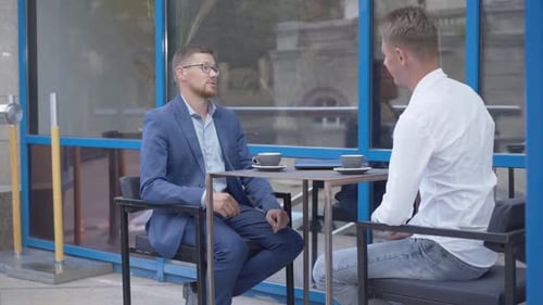 Two Happy Caucasian Businessmen Shaking Hands and Talking at the Table in Outdoor Cafe, Successful