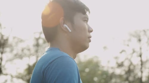 Asian man using wireless earphones on running outdoors at the park. Active lifestyle concept.