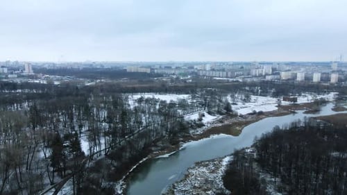 Flight over the river in a snow-covered city park. Aerial photography.