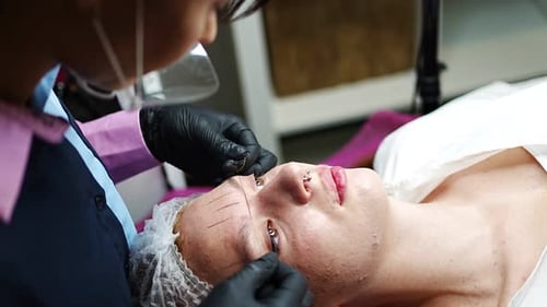 Der Master der Permanent Make-up-Kosmetologin nimmt Messungen für die neue Form der Augenbrauen des Modells vor
