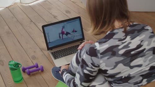 Vista trasera de una mujer bonita y deportiva viendo un Vídeo tutorial de acondicionamiento físico en línea en una computadora portátil en casa