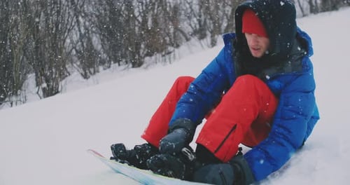 A Man in Red Pants Sitting on the Snow Fastens Snowboard Boots on the Ski Slope