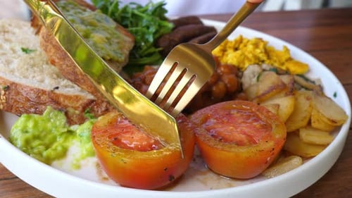 Cutting Tomato on Breakfast Plate with Toast and Eggs