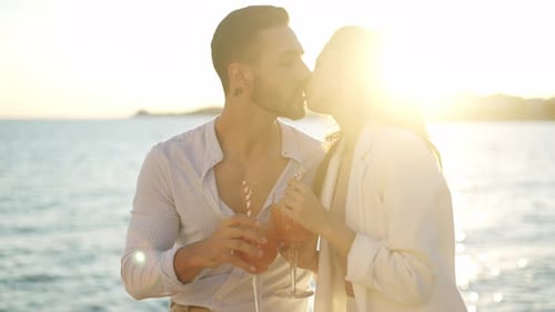 Smiling Hispanic Couple with Cocktails Kissing Against Sea