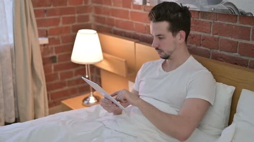 Young Man Using Tablet in Bed
