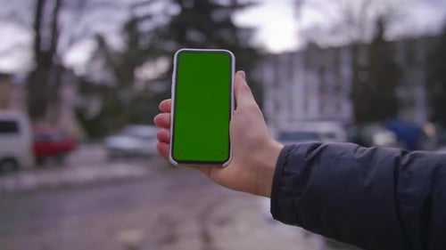 Hand Man benutzt das Halten eines Mobiltelefons mit vertikalem Greenscreen-Hintergrund auf Straßenhäusern