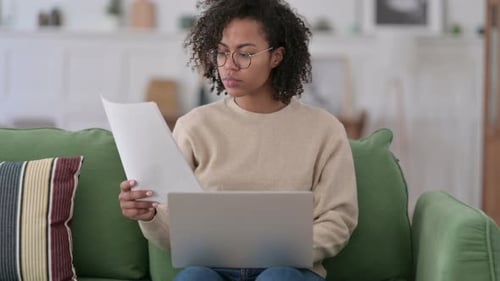 Woman Reading Paper Working on Laptop at Home
