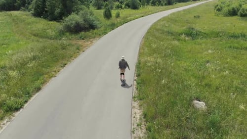 Man Rides at Straight Road on Longboard at Sunset Time Aerial . The Guy Rides a Longboard on the Way