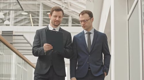 Businessmen Discussing Documents Walking in Modern Office