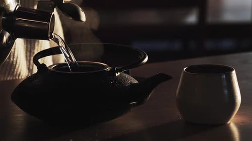 Pouring Water into Teapot with Steaming Cup