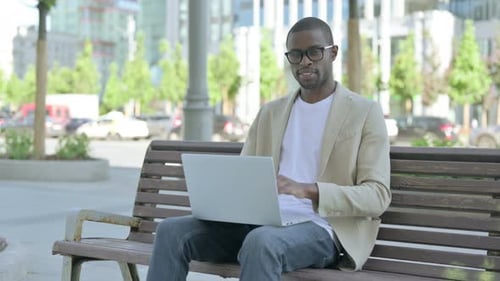 Man Using Laptop on Park Bench in City