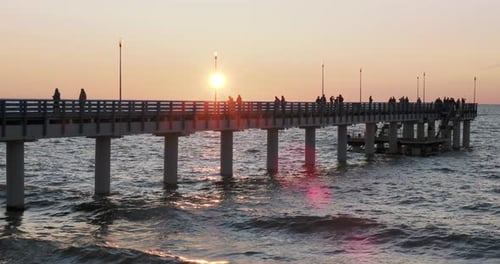 Silhouettes of People Walking on the Pier Against the Sunset. Local People Are Fishing, Tourists Are