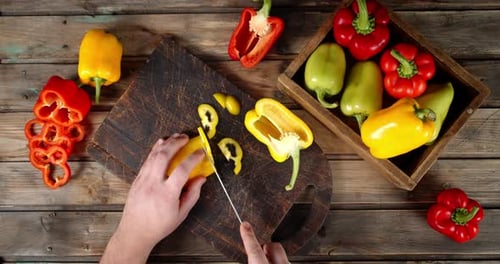Hands Cutting Yellow Pepper on Wooden Board