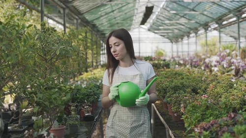 Woman Gardening With Watering Can in Tropical Greenhouse