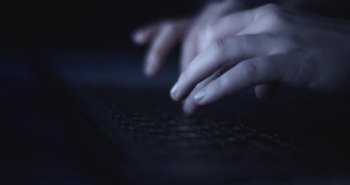 Hands typing on laptop at night