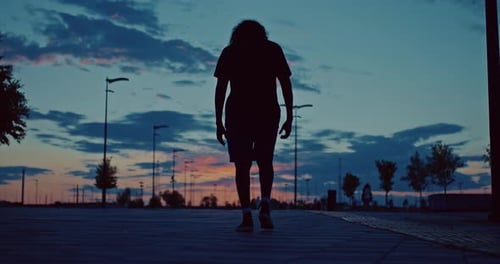 Person Walking Away in Urban Park at Sunset