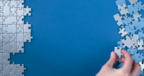 Hands Assembling Jigsaw Puzzle on Blue Surface