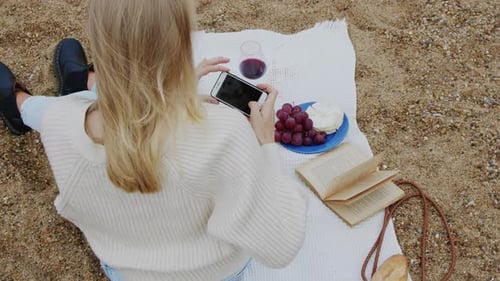 Woman Taking Pictures of Food on Beach Blanket