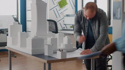 Man Engineer Analyzing Building Model to Design Blueprints Plans on Table