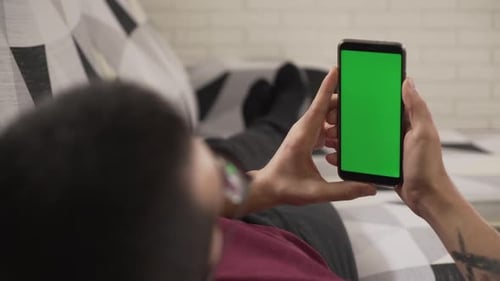 young man lying on the couch staring at his cell phone, green screen