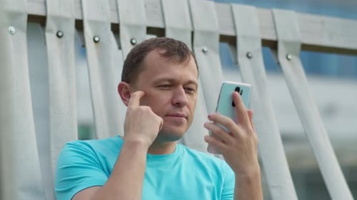 Guy with a Mobile Phone Sitting on a Park Bench Camera Movement Closeup