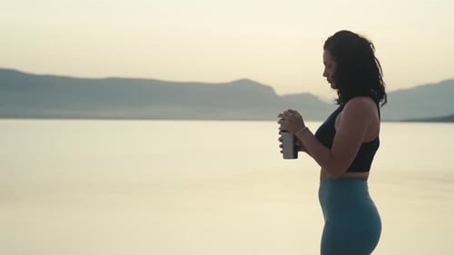 Woman Drinks Water at Beach During Golden Hour