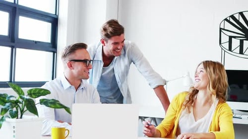 Businesswoman interacting with coworkers while working on laptop