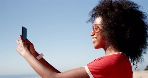 Woman taking selfie with mobile phone on beach in sunshine 4k