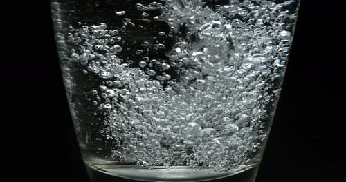 Wasser wird vor schwarzem Hintergrund in Glas gegossen, Zeitlupe 4K