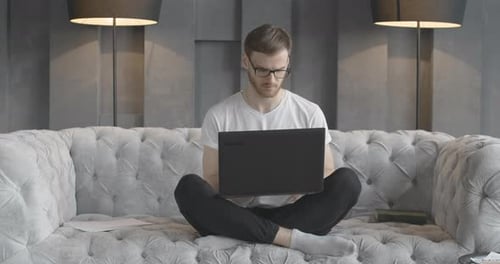 Man Works on Laptop on a Gray Sofa