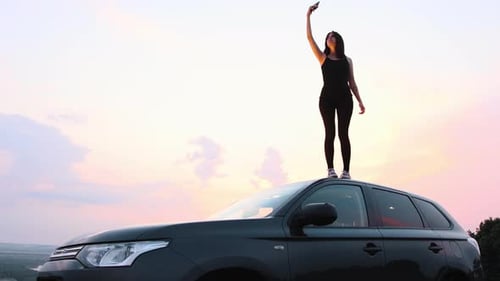 A Young Woman Standing on the Roof of a Car in the Middle of the Field and Trying to Find a Phone