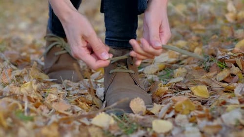 Woman Tying Suede Boots in Autumn Leaves