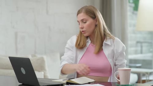 Une femme concentrée est assise à la maison sur le bureau et travaille à l'aide d'un gestionnaire d'ordinateur portable sur un travail à distance pendant