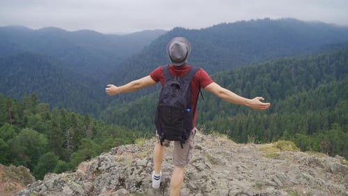 Man Hikes to Mountain Peak Overlooking Green Forest
