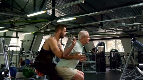 Trainer Helps Senior Man Lift Weights at Gym