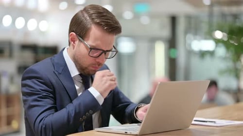 Man Coughing While Working at Laptop in Office