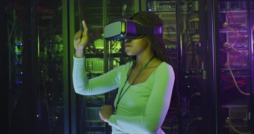 African american female computer technician using vr headset working in business server room