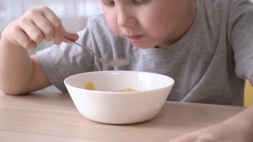 Child Eating Cereal with Spoon at Table