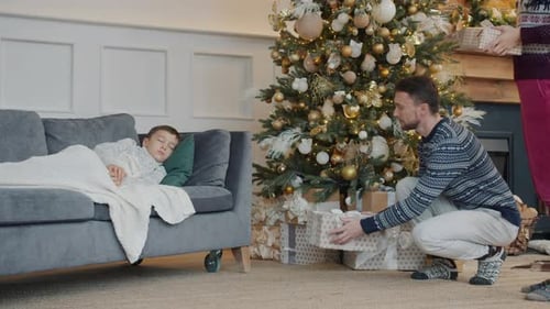 Family Placing Gifts Under Christmas Tree as Boy Sleeps