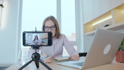 Junge Bloggerin schreibt mit einem Smartphone einen Videoblog, während sie zu Hause in der Küche sitzt.