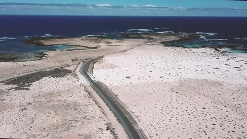Above view of black asphalt road with desert and sand dunes around - coastline with blue ocean