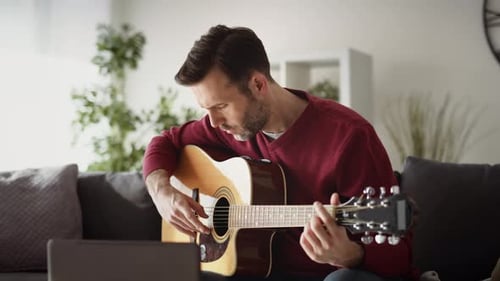 Man Plays Guitar at Home with Sheet Music