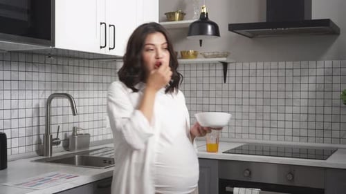 Pregnant Woman Enjoys Healthy Snack in Bright Kitchen