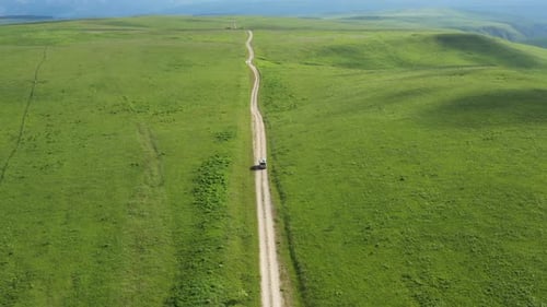 Top view on the driving car of the mountain road through the green field