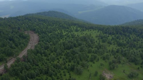 Green forest and rural road on mountains of Manzherok under white clouds