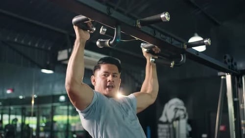 4K Caucasian man bodybuilder pulling up body weight lifting at gym.