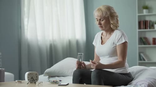 Woman Taking Pill With Water in Bedroom