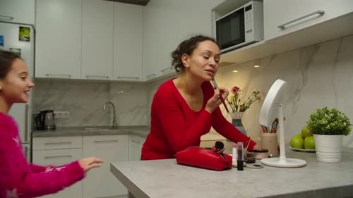 Mother Applies Makeup to Laughing Girl in Kitchen