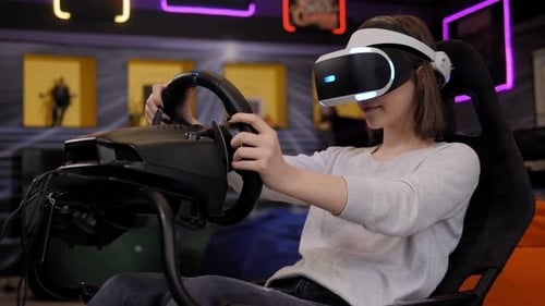 Ein junges Mädchen mit Virtual-Reality-Brille sitzt in einem Auto-Fahrsimulator